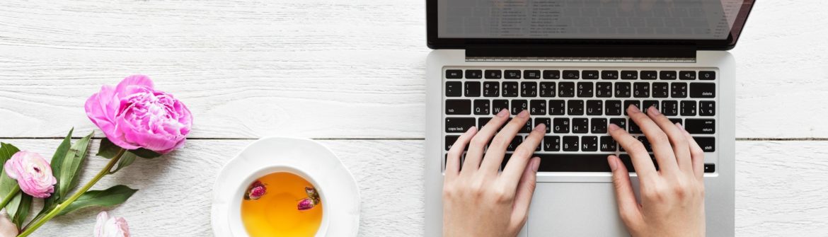 Hands typing on laptop, tea and flowers